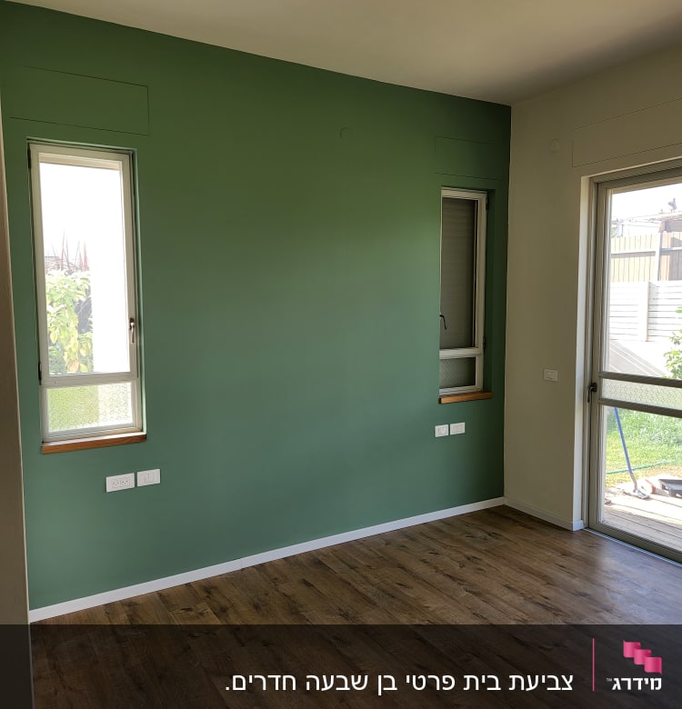 קיר צבוע בירוק עם חלונות ורצפת עץ